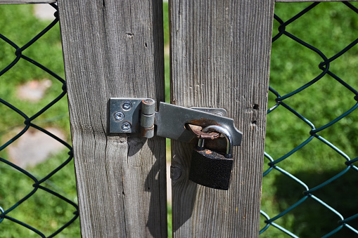 A metal lock hanging on a wooden gate fence door outside.