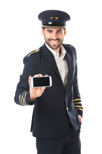 Young man wearing pilot uniform and holding mobile device on white background.