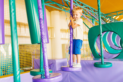 Cute little boy crawling and playing on colorful playground at indoor amusement park