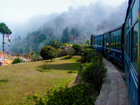 Train passing a beautiful garden and entering into fog. Surrounded by tree covered mountains