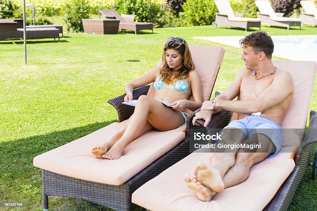 Jeune Couple de détente au bord de la piscine pendant les vacances - Photo de Lire libre de droits