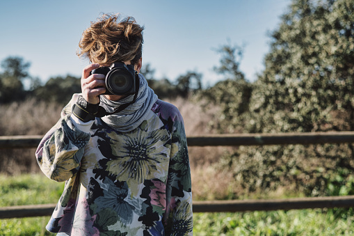 Female Photographer Shooting Outdoors. Portrait Of A Photographer Covering Her Face With Camera. Copy Space