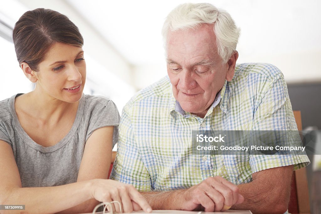 Is this you? Senior man looking at a photo album with his adult daughter Adult Offspring Stock Photo