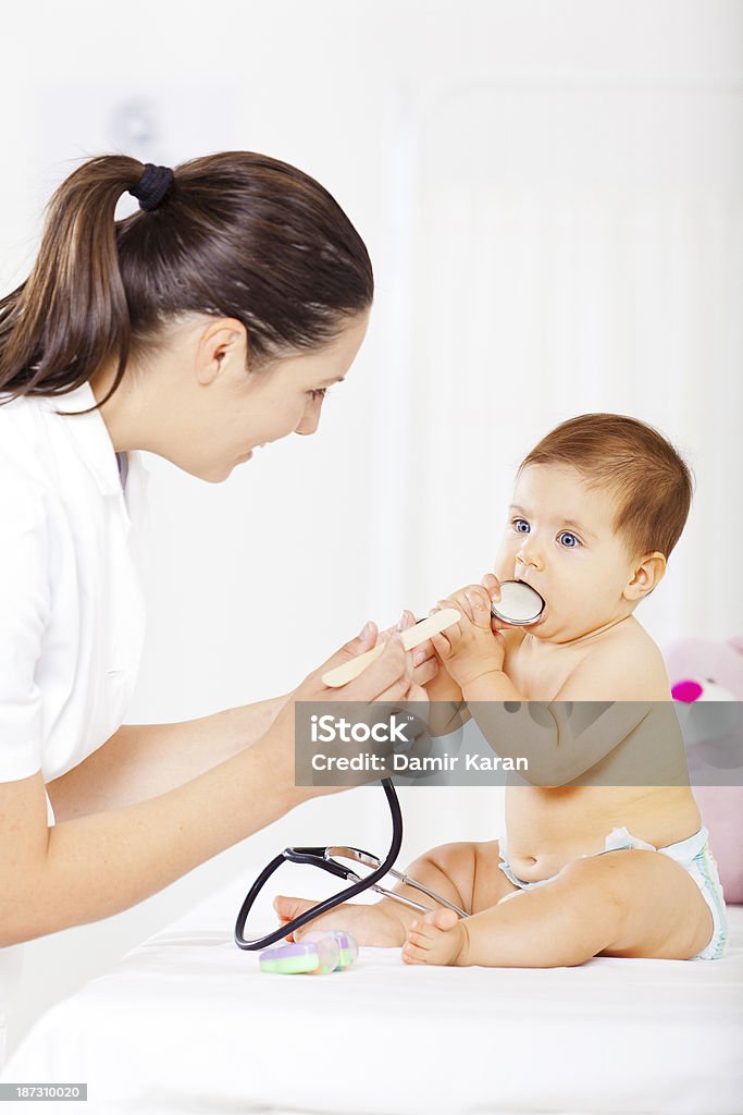 Baby  at pediatrician office Baby girl sitting at pediatrician office, having exam. She is trying to put stethoscope in her mouth while doctor is trying to examine her throat  30-34 Years Stock Photo
