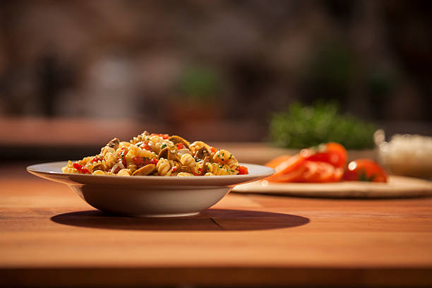 Bowl of Corkscrew Penne pasta primavera fusilli A shallow depth of field image of a bowl of corkscrew pasta primavera in profile view. Image was taken in a kitchen with a butcher block style counter top.  Chopped tomatoes are in the background and out of focus.  Pasta has cheese, spices, herbs, mushrooms, tomatoes and olives in it. empty profile picture stock pictures, royalty-free photos & images