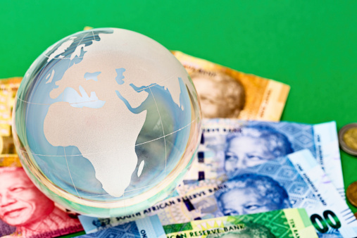 Held down by a crystal globe paperweight, South African banknotes, all featuring the smiling face of iconic statesman Nelson Mandela. The globe shows Africa.