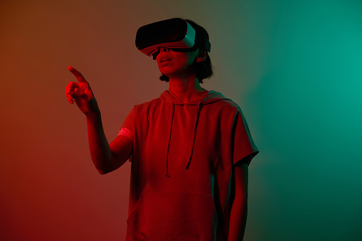 Facial expression of young girl with virtual reality glasses on head in red and green neon in studio
