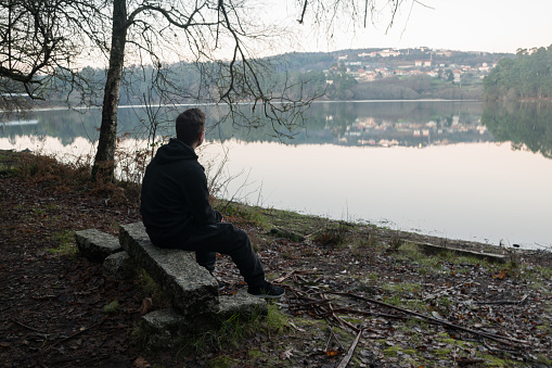 Young boy sitting on the shore of a lake looking at the horizon