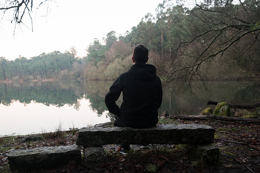 Man sitting on a rock admiring the view of the lake in the forest