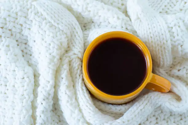 Cup of coffee and cosy woolen sweater on a cold winter morning. Top view. Weekend relaxation and comfort at home.