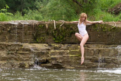 A girl in a white T-shirt, sitting in a stream of water.