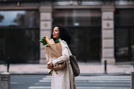 Happy shopper in the city with fresh produce and a bouquet.