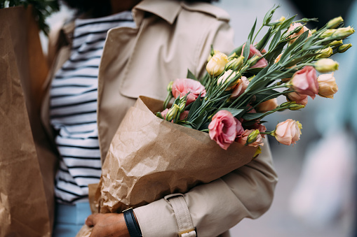 Close up of a woman carrying bags of groceries and a vibrant bouquet on the street.