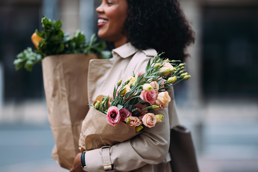 Happy shopper in the city with fresh produce and a bouquet.