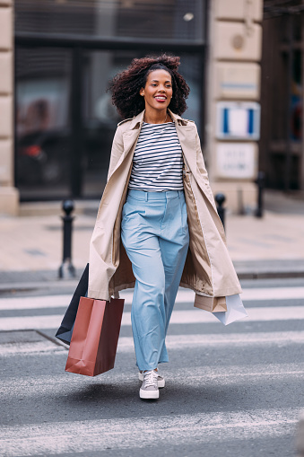 City chic haul: A woman smiles as she carries her shopping bags, showcasing her fashionable finds.