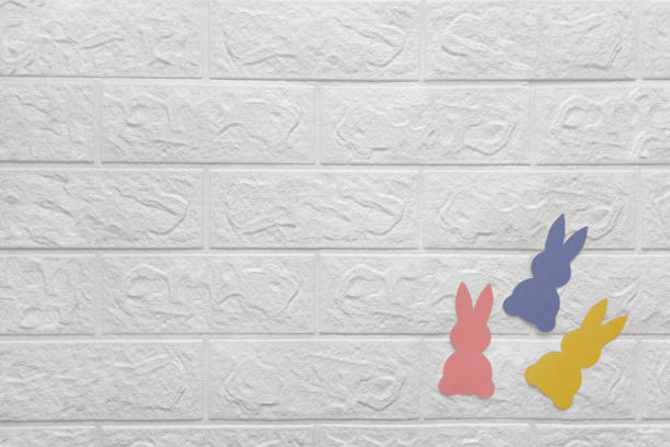 istock Three colored paper rabbits on white brick wall. Place for text. 1873165616