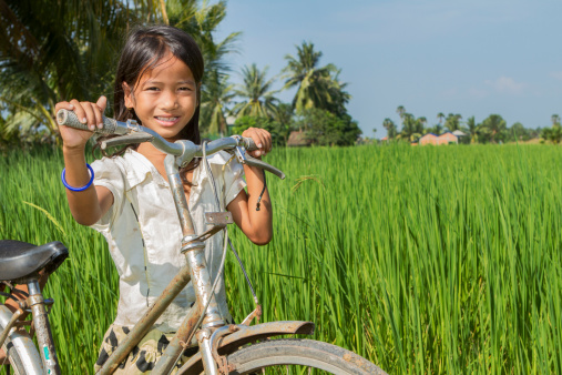 Young Asian (Cambodian) girl with her bicycle in the rice field.