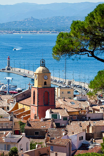 St Tropez French Riviera Across the rooftops to the iconic church tower of  Notre Dame of the Assumption church in St Tropez on the Cote D’Azur. Beyond the harbour and across the the Gulf of Saint Tropez, lies the 1960’s holiday village creation, Port Grimaud and on the hilltop peak behind, the perched 11th century village of Grimaud with it’s castle. pinus pinea photos stock pictures, royalty-free photos & images