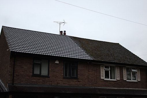 Two semi detached houses, one with a clean roof other with moss growing on roof, taken on an overcast rainy day