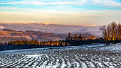 Frozen ploweed field with snow remnants on sunny winter evening. Scenic view of Giant Mountains, Czech: Krkonose, Czech Republic