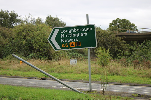 Road sign with broken bent pole on a city roundabout sign leaning slightly