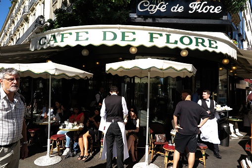 Paris, France - Oct. 1, 2023:  Waiters in white aprons and bow ties ply their trade at the Cafe de Flore, historically a hangout for writers, philosophers and other artists, in the Saint Germain district on the Left Bank of the Seine River.