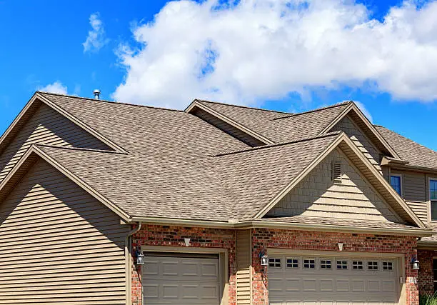 Photo of new asphalt shingles on a two story home. Blue sky and clouds are in the background.