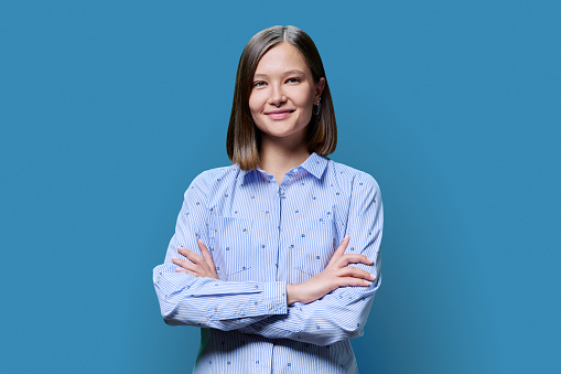 Portrait of confident successful young woman with crossed arms looking at camera on blue studio background. 20s age people, youth, work, education, fashion, lifestyle concept
