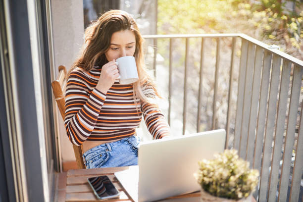 istock Young woman using laptop computer on the terrace of her house while drinking coffee from the cup. 1873205062