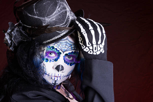 istock Woman in sugarskull makeup touching hat with skeleton glove. 187321600
