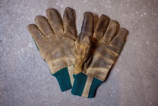 Pair of dirty old yellow and green work gloves on a cement basement floor.