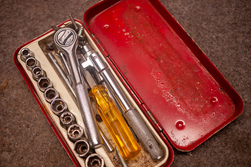 Vintage metal socket wrench set in an old metal painted box on a workbench.