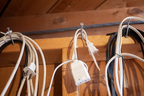 Old black and white electrical extension cords hanging on nails in the wall of a basement workshop.