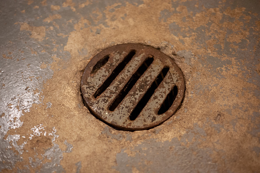 Dirty vintage drain cover in the cement floor of a Canadian basement.