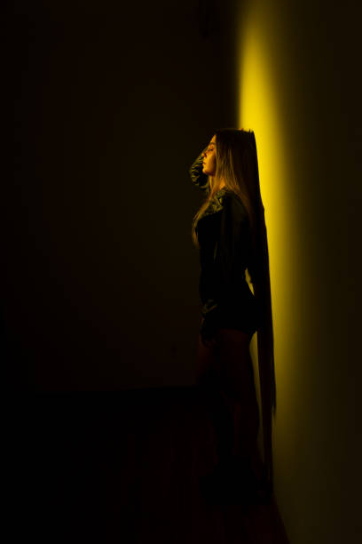 istock A young model woman leaning against a yellow -illuminated wall. 1873239398