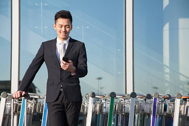 Traveler looking at cellphone next to row of luggage carts Traveler looking at cellphone next to row of luggage carts business person one man only blue standing stock pictures, royalty-free photos & images