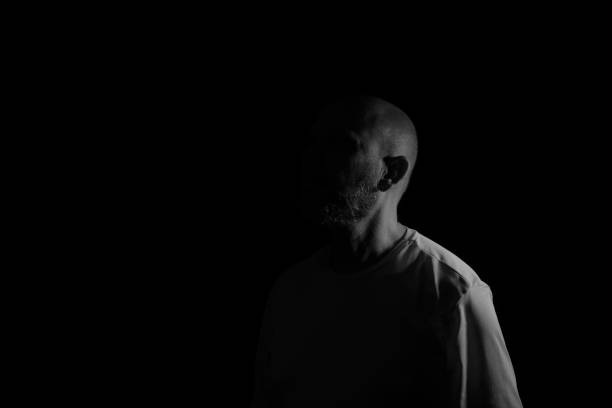 Low light portrait of bearded, bald man. Dark background