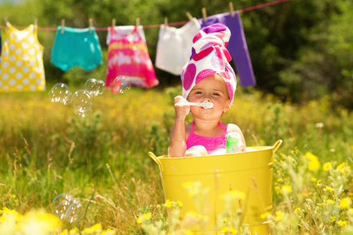 Little girl playing in a metal bathtub with cloths line in background