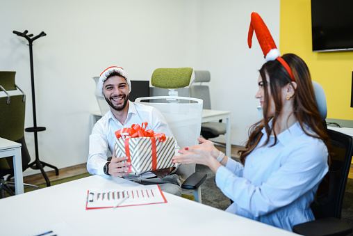 Smiling Male Receiving Christmas Gift By Female Colleague In Office