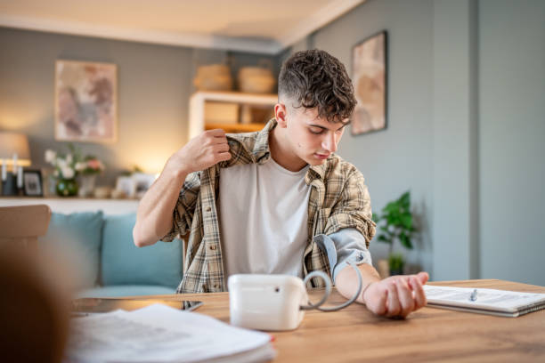 a young student measures his blood pressure, checks his health and the amount of stress while studying for an exam - blood pressure gauge medical exam healthcare and medicine equipment foto e immagini stock