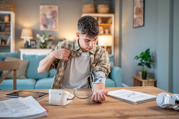 un giovane studente misura la sua pressione sanguigna, controlla la sua salute e la quantità di stress mentre studia per un esame - blood pressure gauge medical exam healthcare and medicine equipment foto e immagini stock