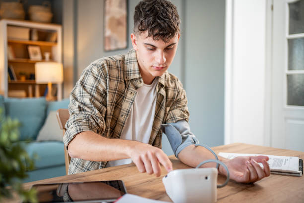 a young student measures his blood pressure, checks his health and the amount of stress while studying for an exam - blood pressure gauge medical exam healthcare and medicine equipment foto e immagini stock