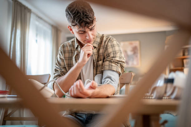 un giovane studente misura la sua pressione sanguigna, controlla la sua salute e la quantità di stress mentre studia per un esame - blood pressure gauge medical exam healthcare and medicine equipment foto e immagini stock