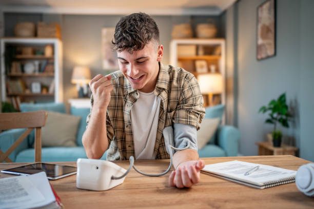 un giovane studente misura la sua pressione sanguigna, controlla la sua salute e la quantità di stress mentre studia per un esame - blood pressure gauge medical exam healthcare and medicine equipment foto e immagini stock