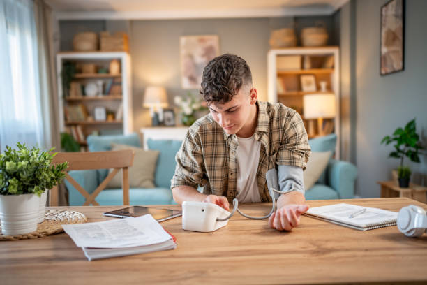 a young student measures his blood pressure, checks his health and the amount of stress while studying for an exam - blood pressure gauge medical exam healthcare and medicine equipment foto e immagini stock