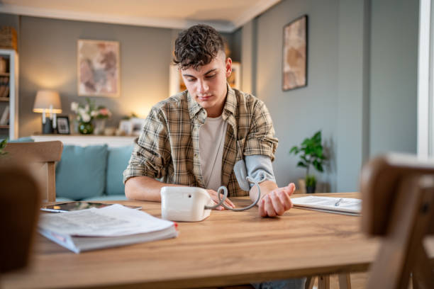 a young student measures his blood pressure, checks his health and the amount of stress while studying for an exam - blood pressure gauge medical exam healthcare and medicine equipment foto e immagini stock