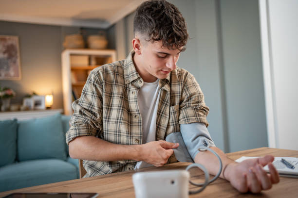 a young student measures his blood pressure, checks his health and the amount of stress while studying for an exam - blood pressure gauge medical exam healthcare and medicine equipment foto e immagini stock