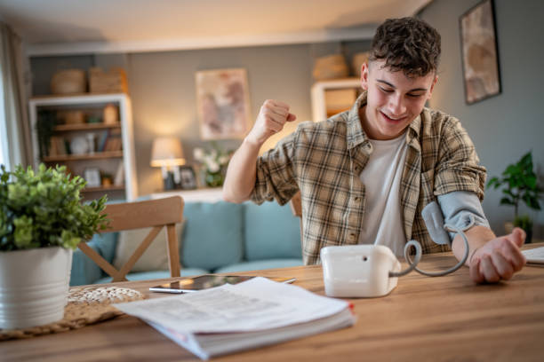 a young student measures his blood pressure, checks his health and the amount of stress while studying for an exam - blood pressure gauge medical exam healthcare and medicine equipment foto e immagini stock