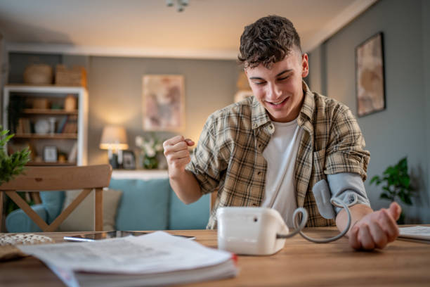 a young student measures his blood pressure, checks his health and the amount of stress while studying for an exam - blood pressure gauge medical exam healthcare and medicine equipment foto e immagini stock