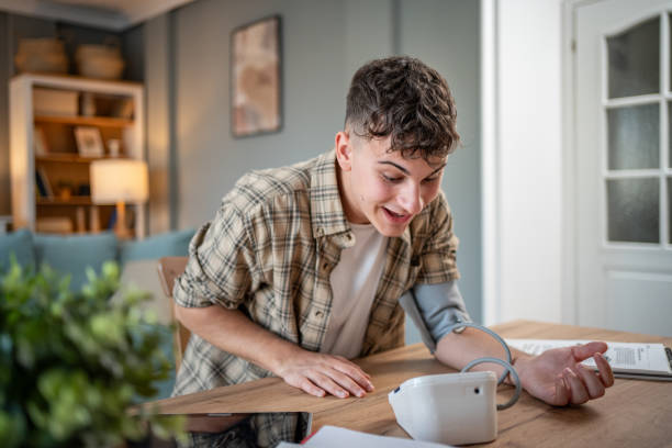 a young student measures his blood pressure, checks his health and the amount of stress while studying for an exam - blood pressure gauge medical exam healthcare and medicine equipment foto e immagini stock